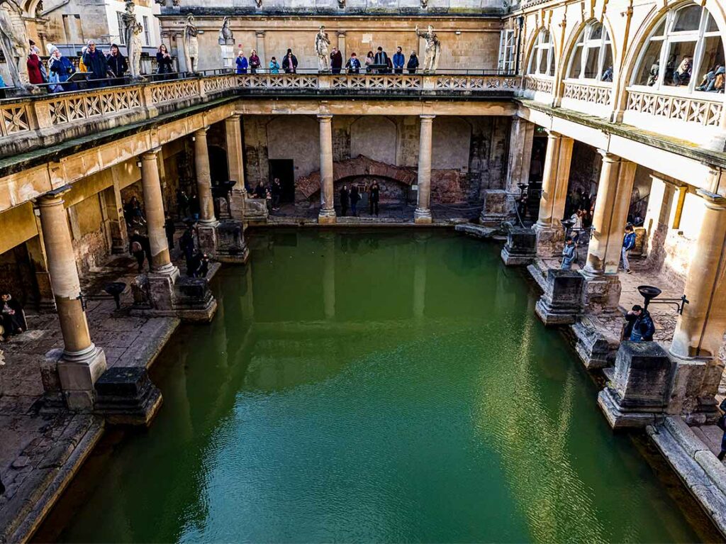 the main bath with people on tour along the side at Roman Baths, in Bath, England,