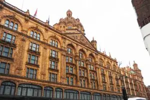 Exterior view of Harrods Department Store in London, showcasing its iconic terracotta facade with elaborate Renaissance-style architecture and multiple flags.