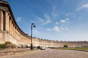 View of the historic Royal Crescent in Bath, England, showcasing its grand Georgian architecture on a sunny day with a clear blue sky, perfect for exploring classic English heritage and architecture.