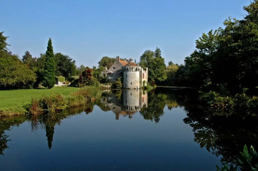 Scotney Castle in England on a serene day, featuring a picturesque reflection on the water surrounded by lush greenery.