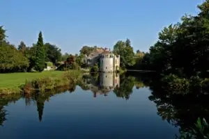 Scotney Castle in England on a serene day, featuring a picturesque reflection on the water surrounded by lush greenery.