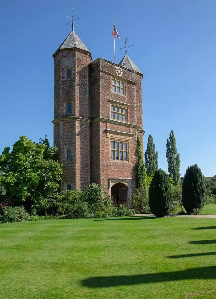 Sissinghurst Castle in England on a sunny day, showcasing its historic brick towers, lush green gardens, and a clear blue sky.