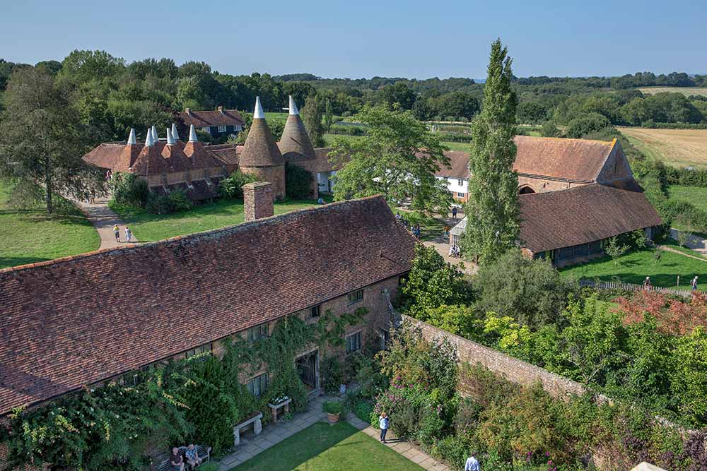 Aerial view of Sissinghurst Castle & Gardens in England, showcasing the historic buildings with iconic conical roofed towers and lush green landscape surrounding the estate.