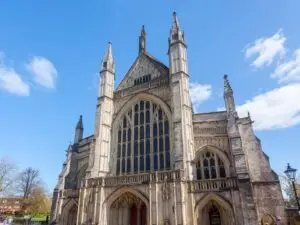 View of the historic Winchester Cathedral in England on a sunny day, showcasing its magnificent Gothic architecture with detailed facades and towering spires against a clear blue sky.