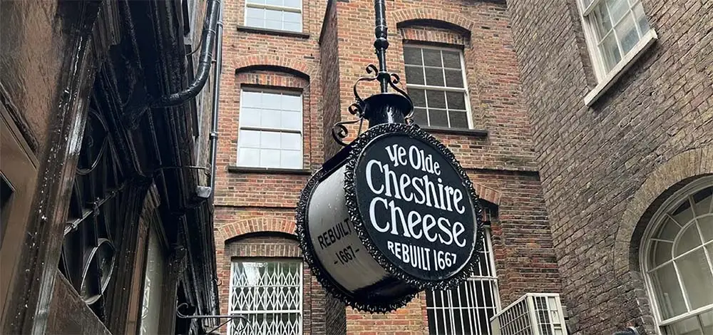 Historic Ye Olde Cheshire Cheese Pub signage in London, England, showing the traditional black and white sign against a backdrop of a classic brick building, highlighting its heritage since 1667.