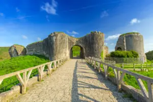 Historic Corfe Castle ruins under a clear blue sky in Dorset, England, viewed from the stone bridge leading to the entrance.