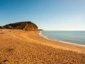 Visitors relaxing on the sandy beach at Jurassic Coast near Charmouth, Dorset with majestic cliffs and calm ocean in the background, a popular British holiday destination