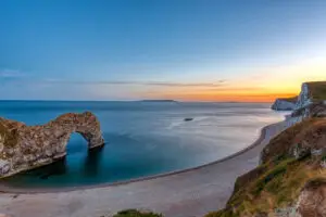 Dusk view of Durdle Door, a natural limestone arch on the Jurassic Coast of Dorset, England, with serene ocean and sunset sky.