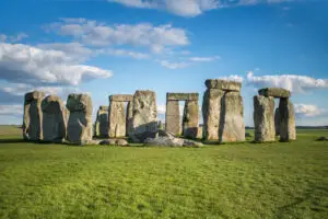 Stonehenge on a sunny day, showcasing the iconic prehistoric megalithic monument on lush green grass under a blue sky with scattered clouds, England.