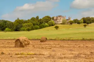 Scenic view of Sherborne Castle in Dorset, England, showcasing the historic architecture amidst a lush landscape with haystacks on a sunny day.