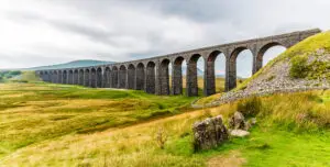 Panoramic summer view of Ribblehead Viaduct in Yorkshire, UK, showcasing its historic arches and surrounding lush greenery.